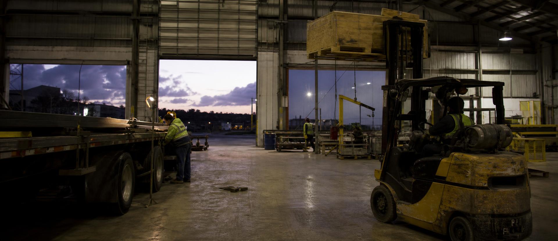 Night shift at a heavy manufacturing plant, workers in hi-vis silhouetted against sparks and steel structure